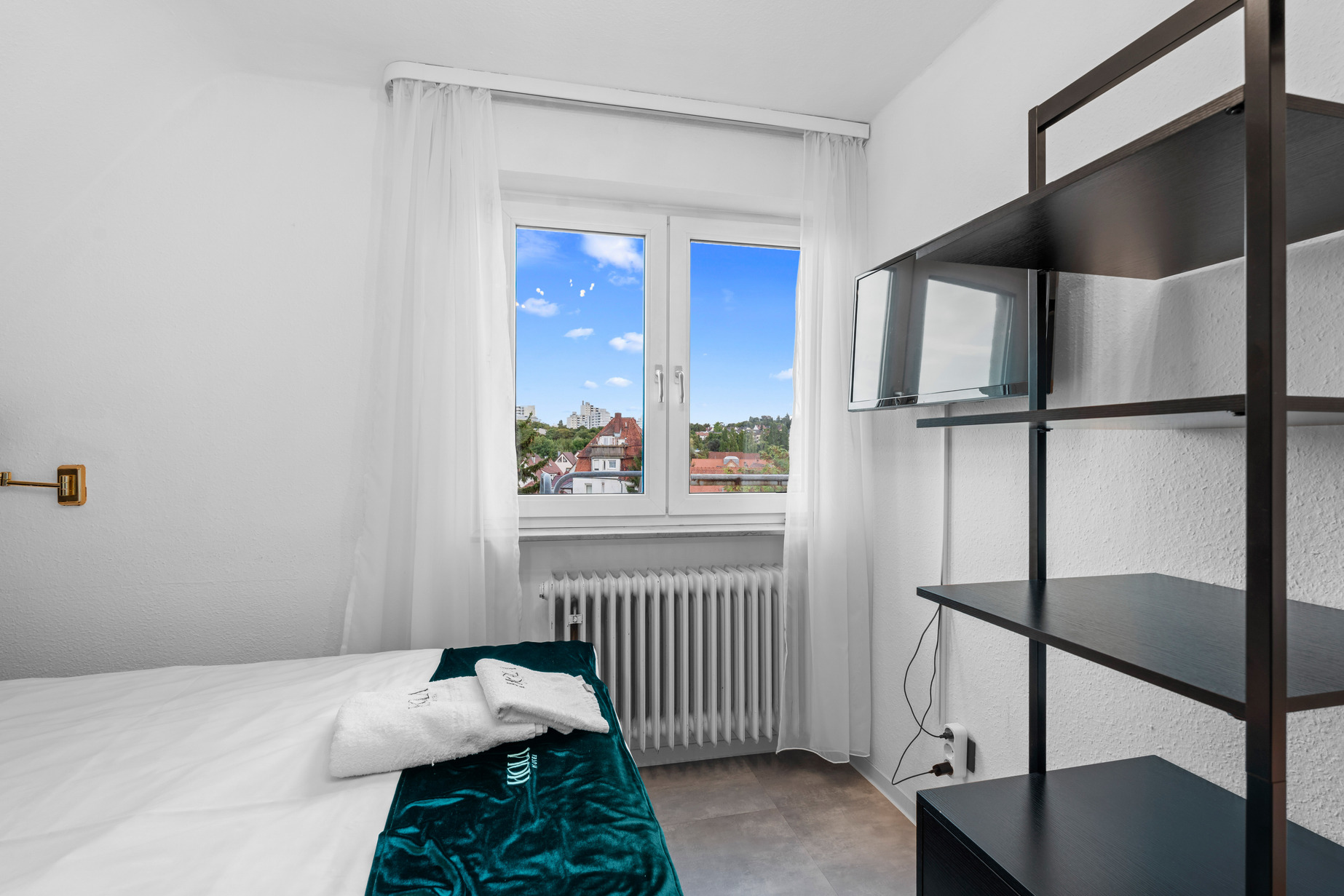 Helles Hotelzimmer im Hola Hotel Stuttgart Zuffenhausen mit Doppelbett und Regal.